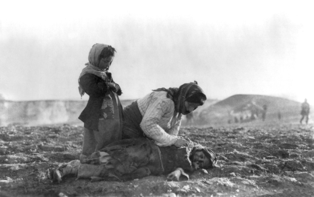 An Armenian woman kneeling beside a dead child in a field within sight of help and safety at Aleppo