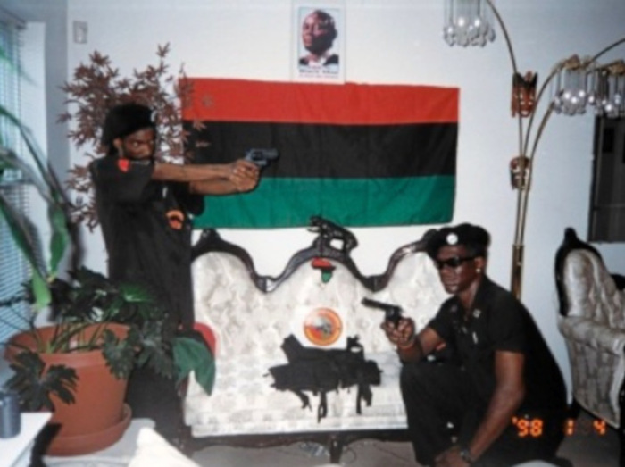 Shebaz and comrade holding guns underneath a picture of Kalid Muhammad