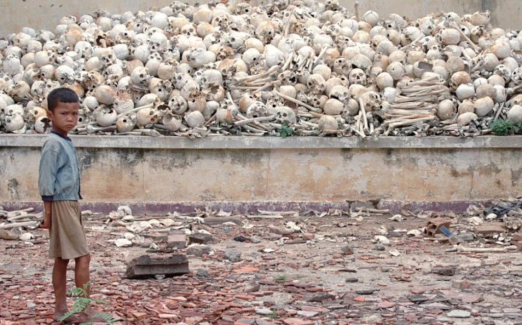 Young Cambodian boy beside hundreds of skulls