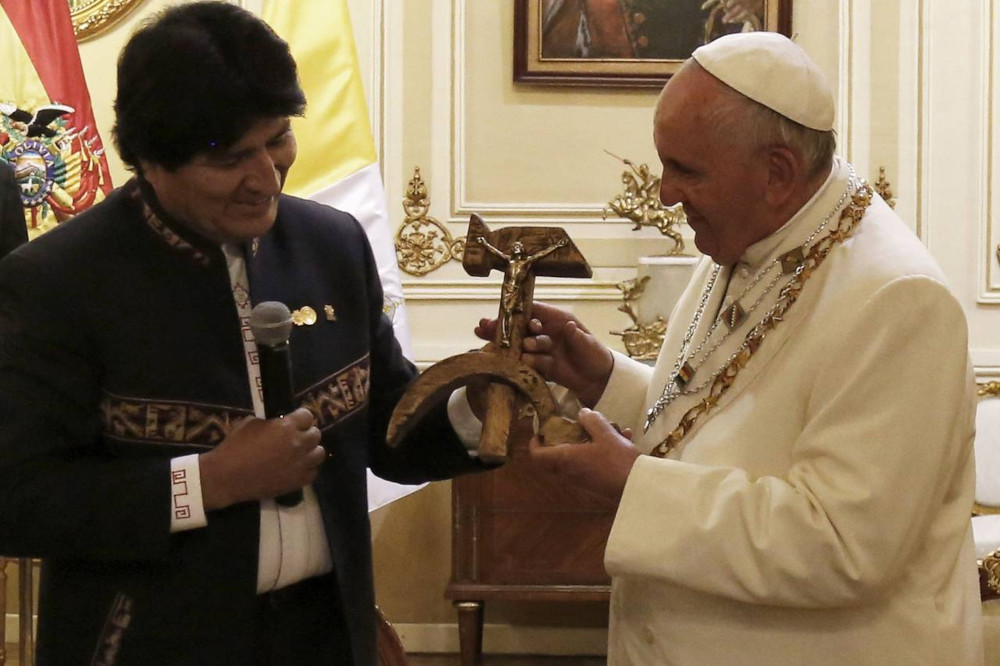 president of bolivia hands pope francis a gift of jesus crucified upon a wooden hammer and sickle