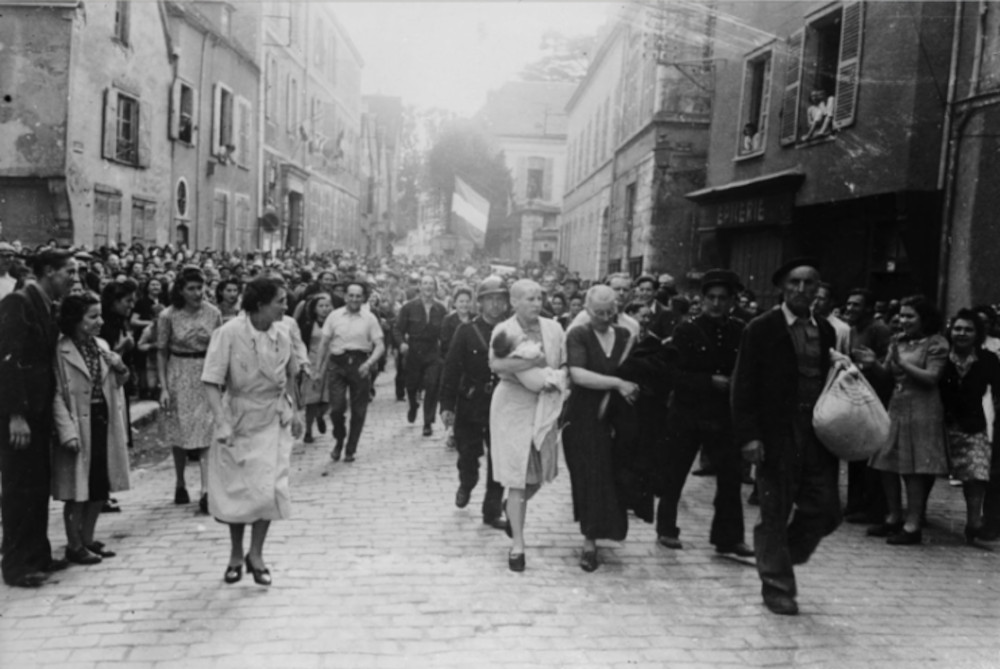 A woman, with her baby whose father is German, and her mother are jeered and humiliated by crowds in Chartres after having their heads shaved as punishment for collaborating with the German troops.